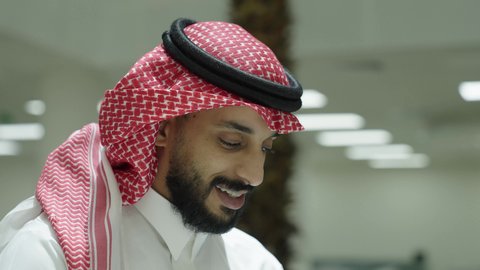 Gestures of joy and happiness, conducting tests and scientific research online, integrating learning with technology, higher education in universities and academic colleges, an Arab Gulf Saudi man wearing traditional attire using a computer inside the university, the quality of university education in the kingdom.
