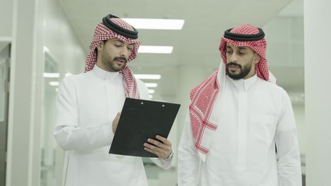 النقاش في المناهج والدروس الجامعية، أستاذ جامعي عربي خليجي سعودي يرتدي الشماغ والثوب التقليدي يمشي مع صديقه لمناقشة امور الطلبة، التعاون بين زملاء المهنة، التعليم العالي الاكاديمي في المملكة العربية السعودية
