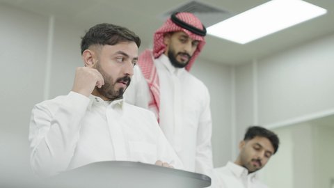 Higher education in the Kingdom of Saudi Arabia, studying and striving for excellence, workshops and training courses, an Arab Gulf Saudi university professor wearing the traditional headscarf and thobe answering a student's question, university students taking exams, taking notes and writing reports.