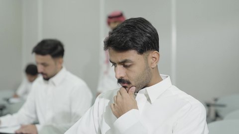 التفكير في الإجابة الصحيحة، الدراسة والاجتهاد من اجل التفوق، ورش عمل ودورات تدريبية، التعليم الجامعي في المملكة العربية السعودية, طالب جامعي عربي خليجي سعودي يرتدي الثوب التقليدي يقوم بتقديم الاختبارات، تدوين وكتابة الملاحظات والتقارير