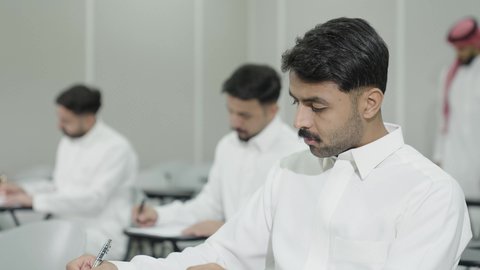 Workshops and training courses, higher education in the Kingdom of Saudi Arabia, an Arab Gulf Saudi university professor wearing the traditional headscarf and thobe supervising students, university students taking exams, taking notes and writing reports, studying and striving for excellence.