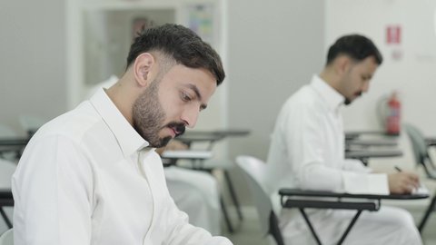 التفكير في الإجابة الصحيحة، الدراسة والاجتهاد من اجل التفوق، ورش عمل ودورات تدريبية، التعليم الجامعي في المملكة العربية السعودية, طالب جامعي عربي خليجي سعودي يرتدي الثوب التقليدي يقوم بتقديم الاختبارات، تدوين وكتابة الملاحظات والتقارير