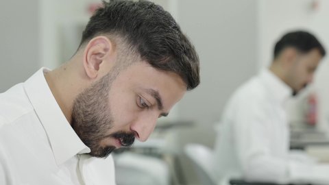 Thinking about the correct answer, studying and striving for excellence, workshops and training courses, higher education in the Kingdom of Saudi Arabia, a Gulf Arab Saudi university student wearing traditional attire taking exams, taking notes and writing reports.