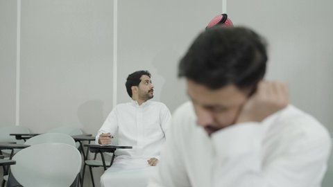السعي للتفوق والنجاح، التعب والاجهاد اثناء حضور المحاضرات اليومية، جودة التعليم العالي في المملكة العربية السعودية، طالب جامعي عربي خليجي سعودي يرتدي الزي التقليدي نائم في الفصل الدراسي، صعوبة الاستيقاظ باكرا