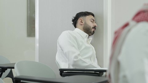 التعب والاجهاد اثناء حضور المحاضرات اليومية، التعليم العالي في المملكة العربية السعودية، السعي للتفوق والنجاح، طالب جامعي عربي خليجي سعودي يرتدي الزي التقليدي نائم في الفصل الدراسي، صعوبة الاستيقاظ باكرا