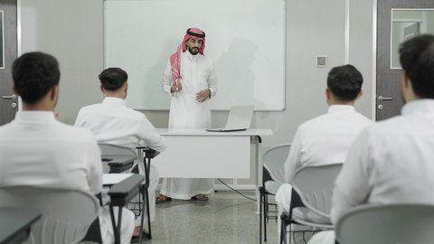 التوضيح والشرح على سبورة بيضاء فارغة، التدريس الفعال في السعودية، التعليم العالي في الجامعات والكليات, دمج التعلم مع التكنولوجيا، أستاذ جامعي عربي خليجي سعودي يرتدي الثوب التقليدي والشماغ يقوم بشرح المعلومات للطلاب، جودة التعليم الجامعي في المملكة العربية السعودية