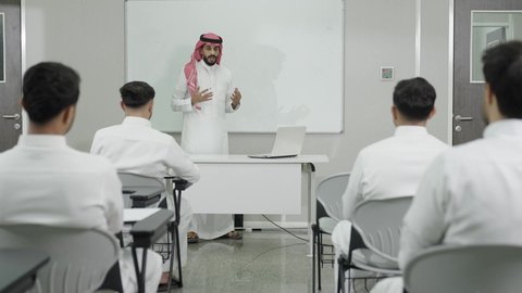 استخدام اللوحة الفصلية البيضاء، التدريس الفعال في السعودية، التعليم العالي في الجامعات والكليات, دمج التعلم مع التكنولوجيا، أستاذ جامعي عربي خليجي سعودي يرتدي الثوب التقليدي والشماغ يقوم بشرح المعلومات للطلاب، جودة التعليم الجامعي في المملكة العربية السعودية