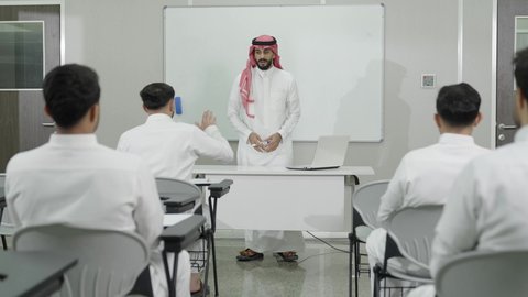 المشاركة الفعالة في الفصل، التدريس الفعال في السعودية، التعليم العالي في الجامعات والكليات, دمج التعلم مع التكنولوجيا، أستاذ جامعي عربي خليجي سعودي يرتدي الثوب التقليدي والشماغ يقوم بشرح المعلومات على الطلاب، جودة التعليم الجامعي في المملكة العربية السعودية