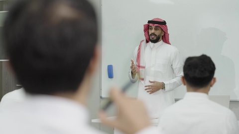 جودة التعليم الجامعي في المملكة العربية السعودية، التعليم العالي في الجامعات والكليات الأكاديمية, دمج التعلم مع التكنولوجيا، اختبارات وكتابة التقارير والأبحاث العلمية، أستاذ جامعي عربي خليجي سعودي يرتدي الثوب التقليدي والشماغ يقوم بشرح المعلومات على الطلاب