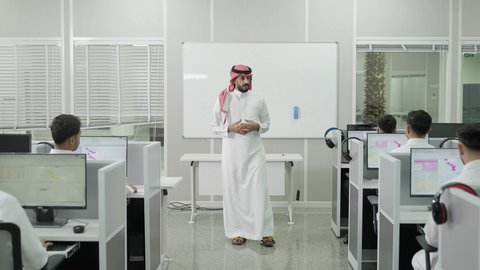 التعليم العالي في الجامعات والكليات الأكاديمية, دمج التعلم مع التكنولوجيا، اختبارات وكتابة التقارير والأبحاث العلمية، أستاذ جامعي عربي خليجي سعودي يرتدي الثوب التقليدي والشماغ يقوم بشرح المعلومات على الطلاب، جودة التعليم الجامعي في المملكة العربية السعودية