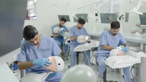 استخدام معدات وأدوات طب الأسنان، الأساليب العلاجية المتبعة للعناية بالفم، معالجة التسوس وتركيب الحشوات، مجموعة من الطلاب الجامعيين بكلية الأسنان يرتدون القفازات يقومون بفحص الأسنان على مجسم