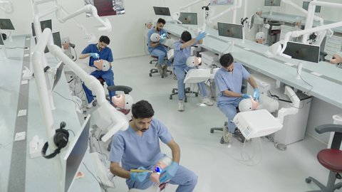 الأساليب العلاجية المتبعة للعناية بالفم، استخدام معدات وأدوات طب الأسنان، معالجة التسوس وتركيب الحشوات، مجموعة من الطلاب الجامعيين بكلية الأسنان يرتدون القفازات يقومون بفحص الأسنان على مجسم
