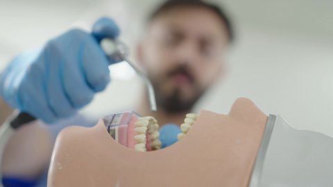 الأساليب العلاجية المتبعة للعناية بالفم، المعدات والادوات اللازمة لإجراء الفحوصات، معالجة النخر والتسوس,تصوير مقرب لطالب جامعي بكلية الأسنان يرتدي القفازات يقوم بفحص مجسم به طاقم أسنان، مفهوم التدريب العملي