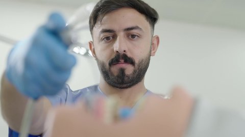 معالجة النخر والتسوس,المعدات والادوات اللازمة لإجراء الفحوصات، تصوير مقرب لطالب جامعي بكلية الأسنان يرتدي القفازات يقوم بفحص مجسم به طاقم أسنان، مفهوم التدريب العملي، الأساليب العلاجية المتبعة للعناية بالفم