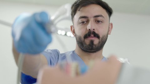 المعدات والادوات اللازمة لإجراء الفحوصات، معالجة النخر والتسوس,تصوير مقرب لطالب جامعي بكلية الأسنان يرتدي القفازات يقوم بفحص مجسم به طاقم أسنان، مفهوم التدريب العملي، الأساليب العلاجية المتبعة للعناية بالفم