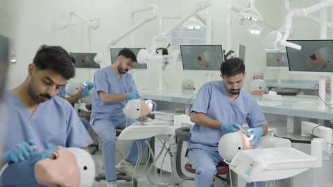 الأساليب العلاجية المتبعة للعناية بالفم، استخدام معدات وأدوات طب الأسنان،معالجة التسوس وتركيب الحشوات، مجموعة من الطلاب الجامعيين بكلية الأسنان يرتدون القفازات يقومون بفحص الأسنان على مجسم