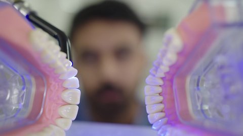 تصوير مقرب لطالب جامعي بكلية الأسنان يرتدي القفازات يقوم بفحص مجسم طاقم أسنان، مفهوم التدريب العملي، استخدام معدات وأدوات طب الأسنان، الأساليب العلاجية المتبعة للعناية بالفم، معالجة التسوس وتركيب الحشوات