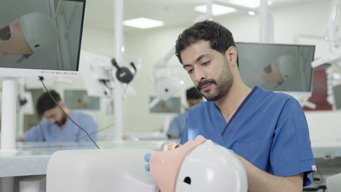 تصوير مقرب لطالب جامعي بكلية الأسنان يرتدي القفازات يقوم بفحص مجسم طاقم أسنان، مفهوم التدريب العملي، المعدات والادوات اللازمة لإجراء الفحوصات، معالجة النخر والتسوس,الأساليب العلاجية المتبعة للعناية بالفم