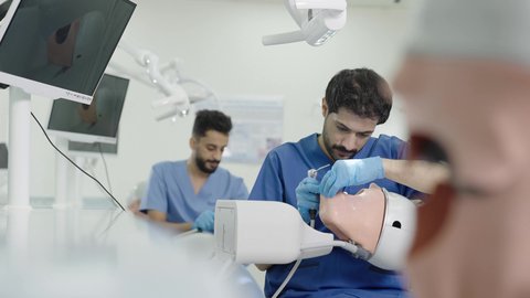 الأساليب العلاجية المتبعة للعناية بالفم، استخدام معدات وأدوات طب الأسنان،معالجة التسوس وتركيب الحشوات، مجموعة من الطلاب الجامعيين بكلية الأسنان يرتدون القفازات يقومون بفحص الأسنان على مجسم