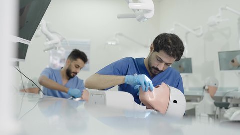 معالجة التسوس وتركيب الحشوات،استخدام معدات وأدوات طب الأسنان، الأساليب العلاجية المتبعة للعناية بالفم،  مجموعة من الطلاب الجامعيين بكلية الأسنان يرتدون القفازات يقومون بفحص الأسنان على مجسم