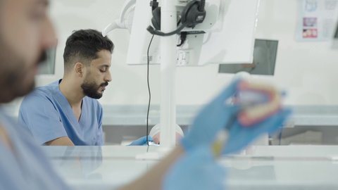 تصوير مقرب لطالب جامعي بكلية الأسنان يرتدي القفازات يقوم بفحص مجسم الأسنان، مفهوم التدريب العملي، استخدام معدات وأدوات طب الأسنان، الأساليب العلاجية المتبعة للعناية بالفم، معالجة التسوس وتركيب الحشوات