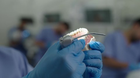 المعدات والادوات اللازمة لإجراء الفحوصات، معالجة النخر والتسوس,تصوير مقرب لطالب جامعي بكلية الأسنان يرتدي القفازات يقوم بفحص طاقم أسنان، مفهوم التدريب العملي، الأساليب العلاجية المتبعة للعناية بالفم