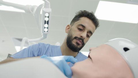 الأساليب العلاجية المتبعة للعناية بالفم، تصوير مقرب لطالب جامعي سعودي بكلية الأسنان يرتدي القفازات يقوم بفحص مجسم طاقم أسنان، مفهوم التدريب العملي، استخدام معدات وأدوات طب الأسنان، معالجة التسوس وتركيب الحشوات 50 وسم