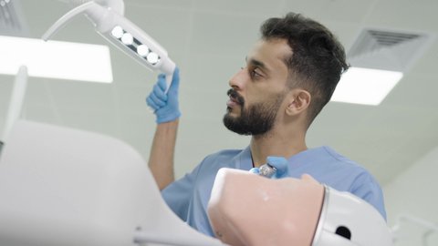 مفهوم التدريب العملي، استخدام معدات وأدوات طب الأسنان، تصوير مقرب لطالب جامعي سعودي بكلية الأسنان يرتدي القفازات يقوم بفحص مجسم طاقم أسنان، الأساليب العلاجية المتبعة للعناية بالفم، معالجة التسوس وتركيب الحشوات 50 وسم