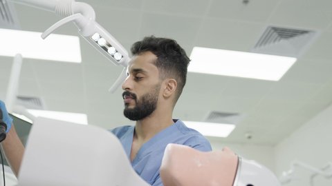 استخدام معدات وأدوات طب الأسنان، الأساليب العلاجية المتبعة للعناية بالفم، تصوير مقرب لطالب جامعي سعودي بكلية الأسنان يرتدي القفازات يقوم بفحص مجسم طاقم أسنان، مفهوم التدريب العملي، معالجة التسوس وتركيب الحشوات 50 وسم