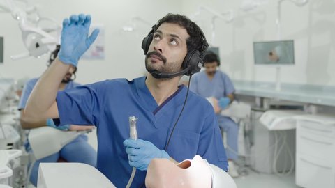 تصوير مقرب لطالب جامعي سعودي بكلية الأسنان يرتدي القفازات يقوم بفحص مجسم طاقم أسنان، مفهوم التدريب العملي، استخدام معدات وأدوات طب الأسنان، الأساليب العلاجية المتبعة للعناية بالفم، معالجة التسوس وتركيب الحشوات 50 وسم