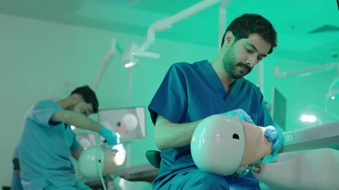 الأساليب العلاجية المتبعة للعناية بالفم، استخدام معدات وأدوات طب الأسنان، معالجة التسوس وتركيب الحشوات، مجموعة من الطلاب الجامعيين بكلية الأسنان يرتدون القفازات يقومون بفحص الأسنان على مجسم