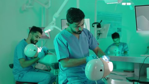 استخدام معدات وأدوات طب الأسنان، الأساليب العلاجية المتبعة للعناية بالفم، معالجة التسوس وتركيب الحشوات، مجموعة من الطلاب الجامعيين بكلية الأسنان يرتدون القفازات يقومون بفحص الأسنان على مجسم