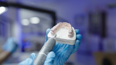 تصوير مقرب ليد طالب جامعي سعودي بكلية الأسنان يرتدي القفازات يقوم بفحص مجسم طاقم أسنان، مفهوم التدريب العملي، استخدام معدات وأدوات طب الأسنان، الأساليب العلاجية المتبعة للعناية بالفم، معالجة التسوس وتركيب الحشوات 50 وسم