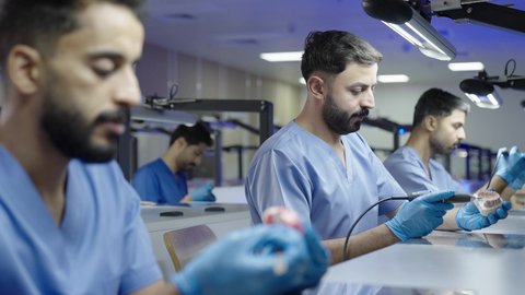 الأساليب العلاجية المتبعة للعناية بالفم، استخدام معدات وأدوات طب الأسنان، معالجة التسوس وتركيب الحشوات، مجموعة من الطلاب الجامعيين بكلية الأسنان يرتدون القفازات يقومون بفحص الأسنان على مجسم