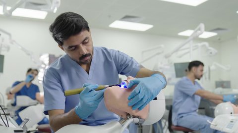 استخدام معدات وأدوات طب الأسنان، معالجة التسوس وتركيب الحشوات،الأساليب العلاجية المتبعة للعناية بالفم، مجموعة من الطلاب الجامعيين السعوديين بكلية الأسنان يرتدون القفازات يقومون بفحص الأسنان على مجسم