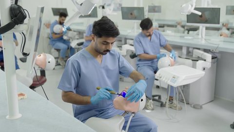 معالجة التسوس وتركيب الحشوات،استخدام معدات وأدوات طب الأسنان، الأساليب العلاجية المتبعة للعناية بالفم، مجموعة من الطلاب الجامعيين بكلية الأسنان يرتدون القفازات يقومون بفحص الأسنان على مجسم