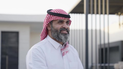 تعابير التقدير واحترام كبار السن, التمسك بالعادات والتقاليد، مفهوم الترابط الأسري وصلة الرحم, أجواء عائلية راقية في الأعياد والمناسبات السعيدة, تصوير مقرب من الجانب لشاب عربي خليجي سعودي يرتدي الزي التقليدي يقوم بتقبيل والده, ايماءات إلقاء التحية والسلام