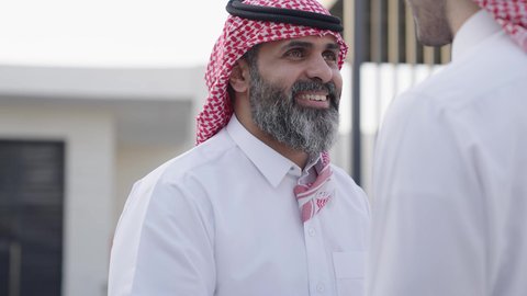 تعابير التقدير واحترام كبار السن, التمسك بالعادات والتقاليد، مفهوم الترابط الأسري وصلة الرحم, أجواء عائلية راقية في الأعياد والمناسبات السعيدة, تصوير مقرب من الجانب لشاب عربي خليجي سعودي يرتدي الزي التقليدي يقوم بتقبيل والده, ايماءات إلقاء التحية والسلام