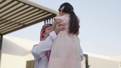 قضاء أوقات ممتعه مع الأهل الأبناء، رجل عربي خليجي سعودي يرتدي الثوب التقليدي والشماغ يرفع ابنته عاليا بإيماءات السعادة، المحافظة على الترابط الأسري، الاعتناء والاهتمام بالاطفال، اللعب والتسلية والترفيه مع العائلة في الهواء الطلق