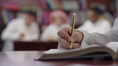 تأدية الواجبات المدرسية، مراجعة الدروس، الإستعداد للعام الدراسي الجديد، التعليم الدراسي في السعودية ، العودة إلى المدارس، المذاكرة للإختبارات المدرسية، تصوير مقرب ليد طالب عربي خليجي سعودي يقوم بحل الدروس المدرسية