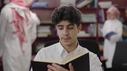 تنمية مهارة القراءة للطلاب، التعليم والدراسة في السعودية ، زيارة مكتبة المدرسة، قضاء وقت الفراغ بالتعلم والتثقف الذاتي، حب الثقافة والاستطلاع، تصوير مقرب لطالب عربي خليجي سعودي يرتدي الثوب الابيض و الشماغ يقوم بقراءة كتاب, الاهتمام بتصفح الكتب المفيدة