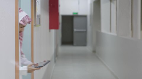 Collaborative study to enhance group learning among peers, the concept of e-learning, discussion of study materials, an Arab Gulf Saudi student wearing a white thobe and a ghutrah with a school bag standing alongside a colleague, using a tablet in studying, using modern technological devices.