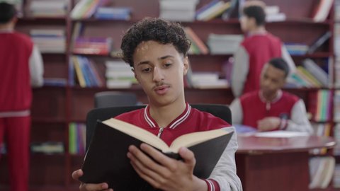 Visiting the school library, love for culture and exploration, a close-up shot of a Saudi Gulf Arab student wearing a school uniform holding a book, developing reading skills for students, education and studying in Saudi Arabia, spending free time learning and self-cultivation.