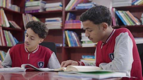 اكاديميات ومدارس حديثة، طلاب عربيين سعوديين خليجيين يرتدون الزي المدرسي يجلسون في المكتبة المدرسية، الاستمتاع بقراءة الكتب المدرسية، تأدية الواجبات المدرسية، التعليم في المملكة العربية السعودية