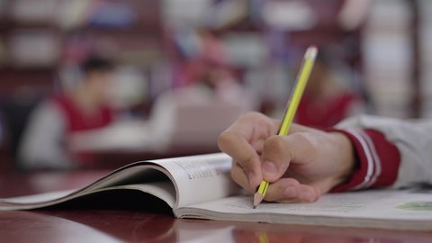 تصوير مقرب ليد طالب يقوم بحل الواجبات المدرسية، حوارات ونقاشات بين الاستاذة والطلاب، معلم عربي خليجي سعودي يرتدي الثوب التقليدي والشماغ يجلس امام الحاسب المحمول يقوم بمناقشة الدروس مع طلابه داخل المكتبة المدرسية