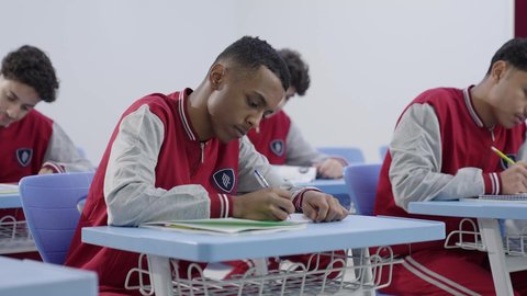 الدراسة و الاجتهاد من اجل التفوق، التربية والتعليم بالمناهج المقررة للطلاب في المملكة العربية السعودية, مجموعه من الطلاب العربيون الخليجيون السعوديون يرتدون الزي المدرسي يقومون بحل اسئلة الامتحان، ايماءات التمعن و التركيز