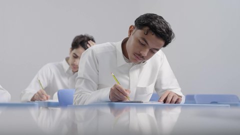 الانجاز و النجاح في المرحلة التعليمية، التعليم في المملكة العربية السعودية، تصوير مقرب لمجموعه من الطلاب العربيون الخليجيون السعوديون يرتدون الثوب الابيض يقومون بحل اسئلة الامتحان بايماءات التركيز والتمعن، اختبارات نهاية الفصل الدراسي