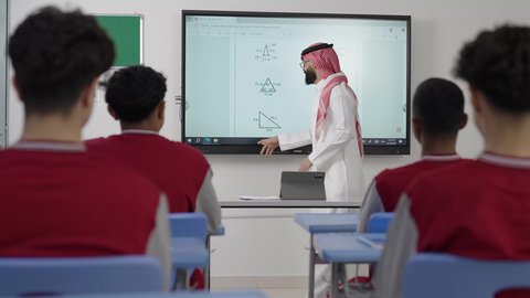 الإهتمام بقدرات التلاميذ بتقديم الدروس،  طلاب عربيين خليجيين سعوديين يجلسون في مقاعدهم وأمامهم مدرس سعودي يستخدم التابلت فى الشرح، المشاركة الفعالة في النقاشات داخل الفصل، الاستفادة من التقنيات المتطورة في التعلم والدراسة، تطور طرائق التدريس في مدارس المملكة