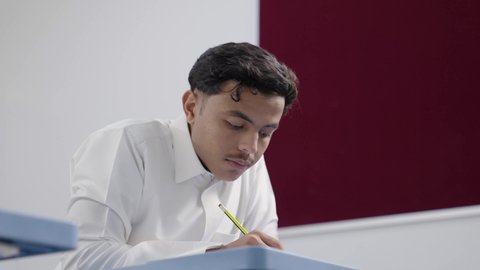 دور العلم في تنمية التفكير الإبداعي والتحليل المنطقي، مفهوم الاجتهاد وطلب التفوق، التربية والتعليم في السعودية، معلم عربي خليجي سعودي يرتدي الثوب الابيض و الشماغ يقوم بمساعدة طالب اثناء تقديم الامتحانات