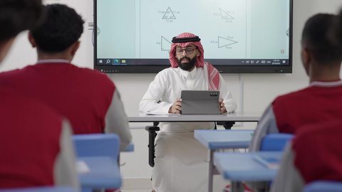 المشاركة والتفاعل داخل الفصل الدراسي،الاستفادة من التقنيات المتطورة في التعلم والدراسة، تطور طرائق التدريس في مدارس المملكة، المناهج المطورة والتعليم الالكتروني، طلاب عربيين خليجيين سعوديين يجلسون في مقاعدهم وأمامهم مدرس سعودي يستخدم التابلت فى الشرح